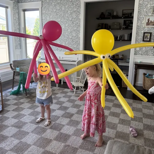 Two kids holding pink and yellow balloon octopus characters